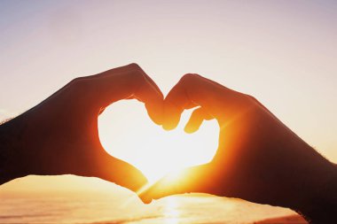 Gökyüzünün arka planında kalp şeklinde bir erkek elleri güneş ışınlarını içeri aldı..