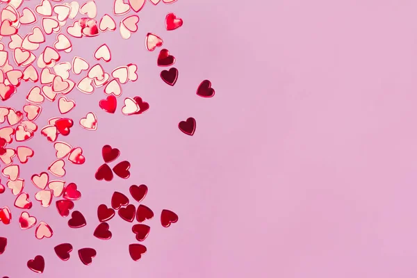 Kleine rode hartvormige confetti op roze achtergrond — Stockfoto