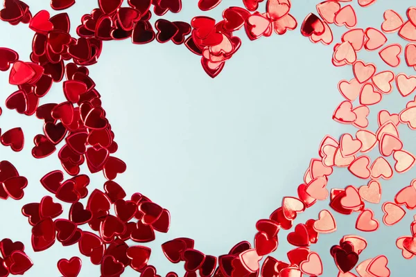 Red foil confetti arranged into a heart shaped frame on blue background. — Stock Photo, Image