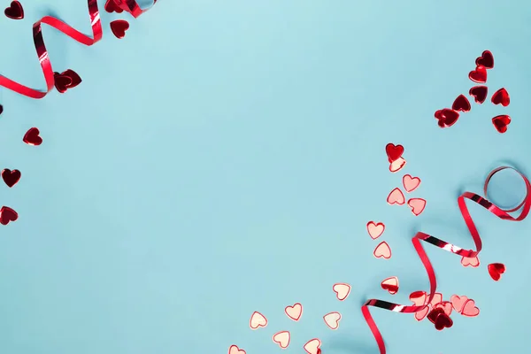 Red heart shaped confetti and curly ribbons on blue background with copy space. — Stock Photo, Image