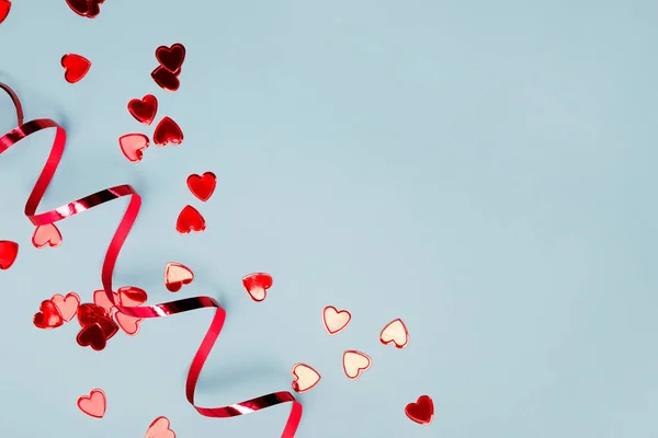 Red heart shaped confetti and ribbon on blue background with copy space. — Stock Photo, Image