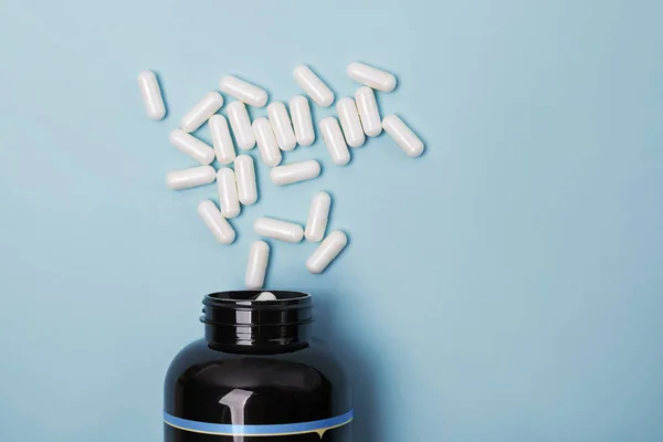 Tarro con píldoras médicas blancas dispersas sobre fondo azul , — Foto de Stock