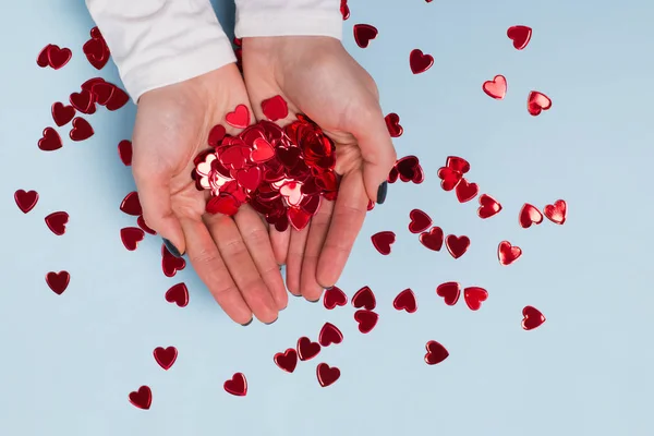 Dłonie kobiecetrzymajążywe czerwone musujące konfetti w kształcie serca — Zdjęcie stockowe