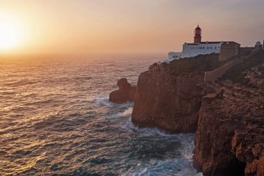Sarı günbatımı diski bir deniz feneriyle okyanusa açılıyor.