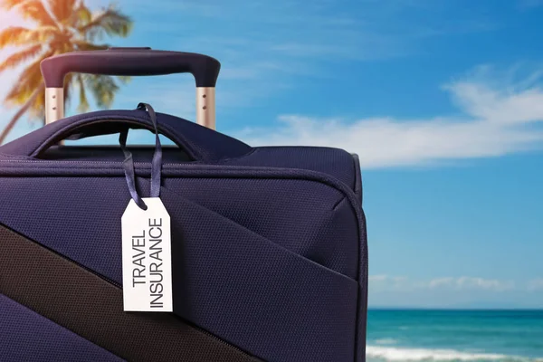 Modrý kufr s cestovní pojištění štítek detailní up — Stock fotografie