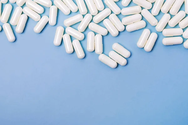 Много белых медицинских таблеток на синем фоне с копировальным пространством — стоковое фото