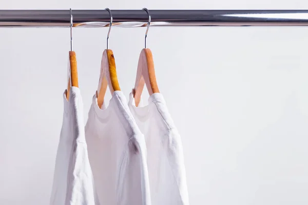 Drie witte t-shirts hangend aan houten hangers — Stockfoto