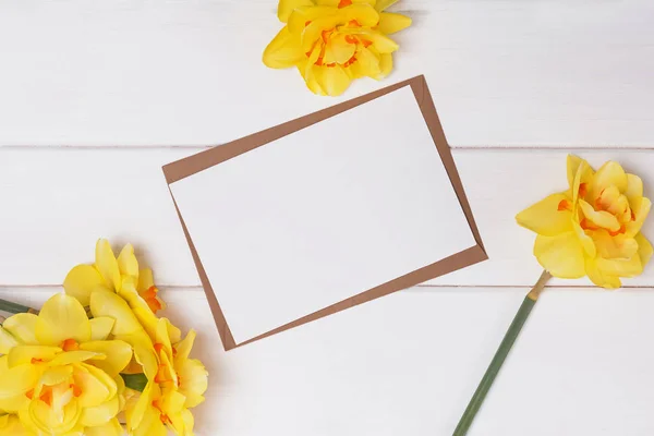 Blank paper and yellow spring flowers on the white wooden table — Stok fotoğraf