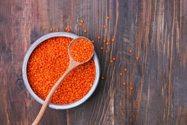 Red lentils in a bowl and spoon on wooden background, top view. — 스톡 사진