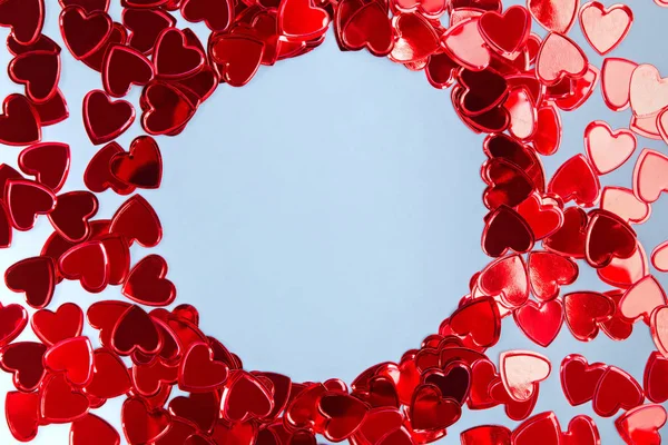 Konfety tvaru srdce uspořádány do kruhového rámu na modrém pozadí. — Stock fotografie