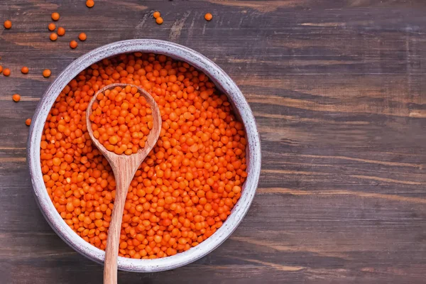 Red lentils in a bowl and spoon on wooden background, top view. — 스톡 사진
