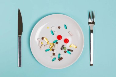 Farklı şekil ve boyutlarda kapsül ve tabletlerle dolu bir tabak.