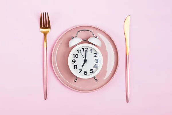 Reloj despertador retro en placa con tenedor y cuchillo aislado sobre fondo rosa . —  Fotos de Stock