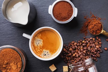 Bir fincan sade kahve, espresso makinesinin filtresi ve kızarmış kahve çekirdekleri.