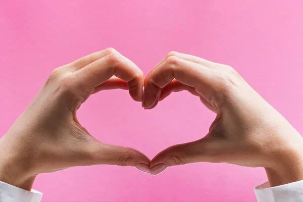 Manos femeninas formando un símbolo del corazón sobre fondo rosa — Foto de Stock