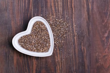Tahta arka planda beyaz kalp şeklinde bir kasede Chia tohumları.