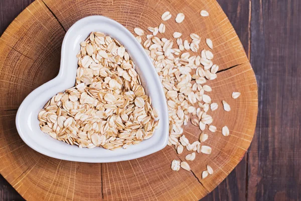Oatmeal in heart-shaped plate on wooden surface — Stock Photo, Image