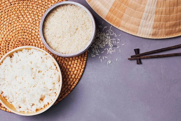 Чаши с сырым и приготовленным белым длинным зерном риса на сером столе — стоковое фото