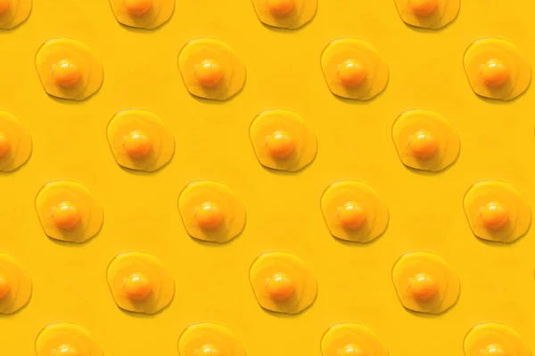 Kreatywny wzór z surowych jaj z żółtkami na żółtym tle. — Zdjęcie stockowe