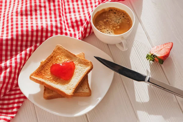 Geroosterde broodschijfjes met jam in hartvorm erop en een kop koffie — Stockfoto