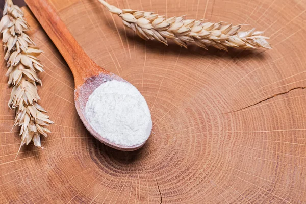 Orelhas de trigo e farinha na colher de madeira na mesa — Fotografia de Stock