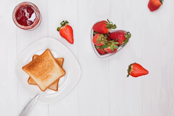 Rebanadas de pan tostado, mermelada de fresa, fresas y café en la mesa blanca . — Foto de Stock