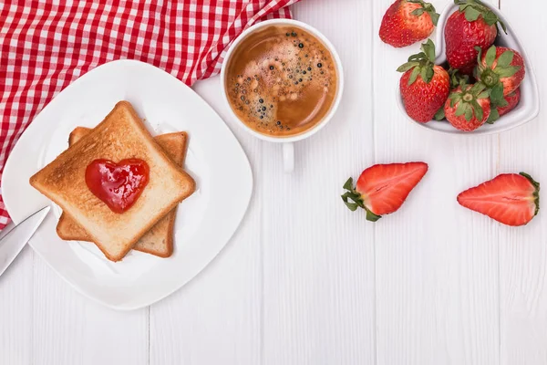 Хлеб и джем в форме сердца, клубника и кофе на белом столе — стоковое фото