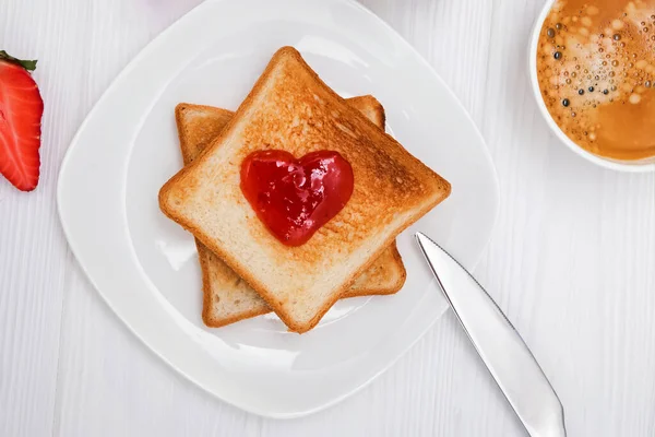 Φρυγανισμένο ψωμί με μαρμελάδα σε σχήμα καρδιάς, φράουλες και καφέ στο λευκό τραπέζι. — Φωτογραφία Αρχείου