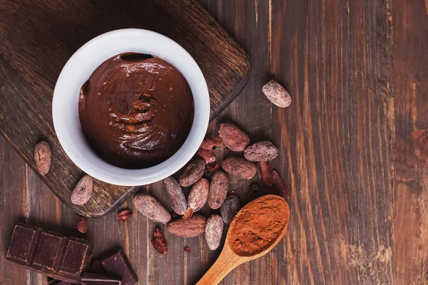 Creme de chocolate, grãos de cacau e pó e pedaços de chocolate na mesa de madeira — Fotografia de Stock