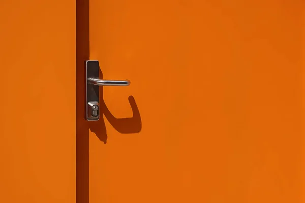 Bright orange metal door with handle close-up. Modern exterior