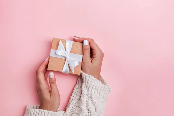 Top view kéz nő gazdaság barna ajándék doboz fehér szalag rózsaszín pasztell szín háttér — Stock Fotó