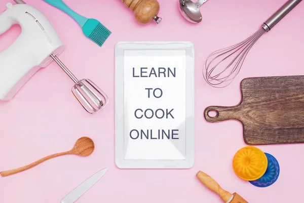 Кухонне начиння та посуд на рожевому столі та планшеті з текстом Вчіться готувати онлайн . — стокове фото