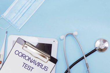Tıbbi maske, termometre ve mavi arka planda diğer tıbbi doktor ekipmanları. Kağıt üzerinde metin covid-19 testi..
