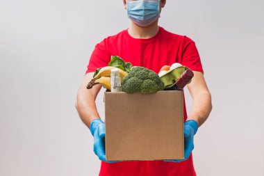 Maske takan teslimatçı ve farklı yiyeceklerle dolu bir kutu tutan eldiven..