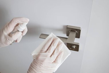 Coronavirus COVID-19 Temizlikçi kadın antibakteriyel dezenfektanla kapı kolunu temizliyor.
