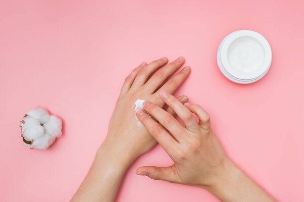 Woman moisturizing her hand with cosmetic cream with copy space on pink background in minimalism style.