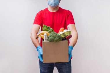Maske takan teslimatçı ve eldivenli bir karton kutu dolusu farklı erzak taşıyor..