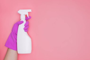 Pembe plastik eldivenli kadın. Elinde pembe arka planda temizlik malzemesi şişesi var..