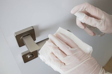 Coronavirus COVID-19 Temizlikçi kadın antibakteriyel dezenfektanla kapı kolunu temizliyor.