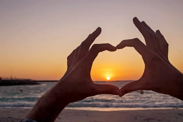 Mężczyzna ręce w kształcie serca na tle zachód słońca — Zdjęcie stockowe