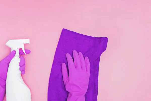 Жіноча рука в гумовій рукавичці тримає чистий спрей і ганчірку на рожевому фоні . — стокове фото