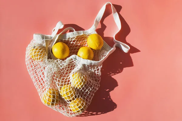 Siatkowa torba na zakupy z cytrynami na różowym tle. Naturalne cienie światła słonecznego — Zdjęcie stockowe