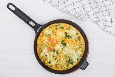 Beyaz masadaki demir tavada sebzeli omlet ya da sebze karışımı bir şey..