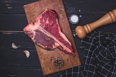 Raw T-bone beef steak on the wooden board and spices on black table. clipart