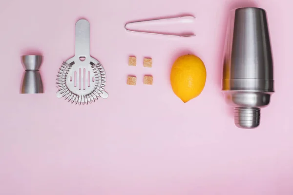 Agitador, jigger y otras herramientas de bar con limón y azúcar sobre fondo rosa — Foto de Stock