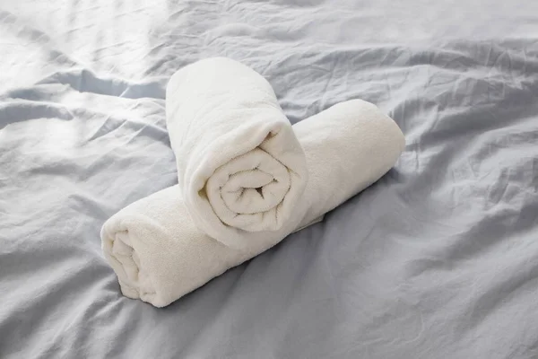 Rolou toalhas limpas brancas na cama com roupa de cama cinza . — Fotografia de Stock