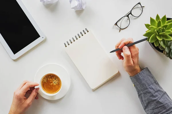 Man som skriver i anteckningsblocket och dricker kaffe på sin arbetsplats — Stockfoto