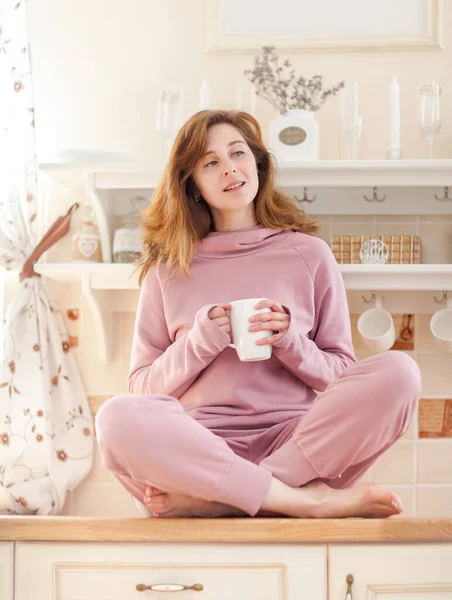 Genç bayan mutfakta bir fincan çayla oturuyor.