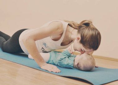 Genç anne bebeğiyle birlikte fiziksel yoga egzersizleri yapıyor.