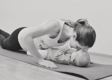 Genç anne bebeğiyle birlikte fiziksel yoga egzersizleri yapıyor.